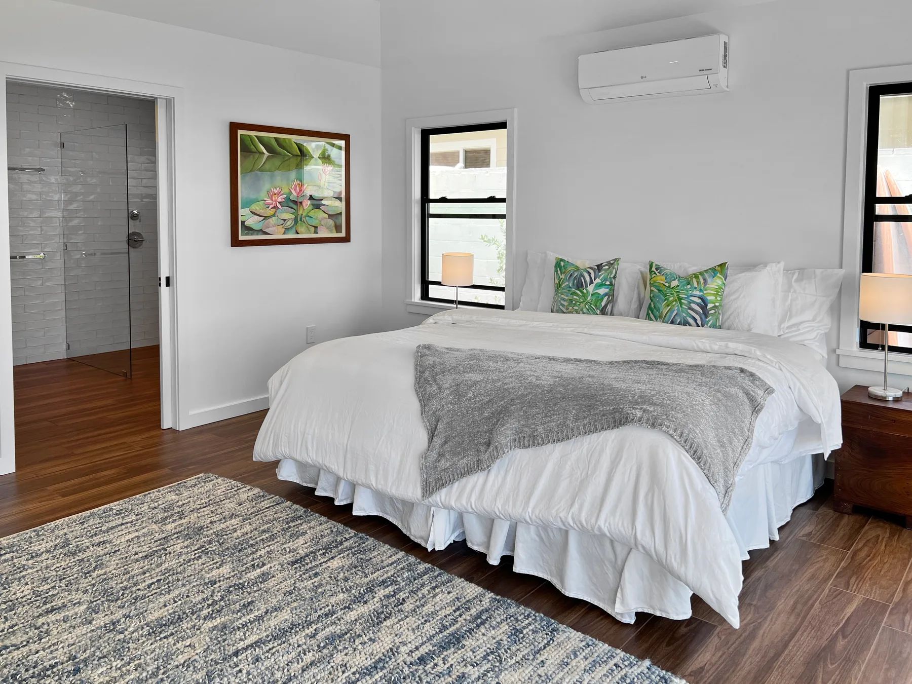 A bright bedroom with a white bed, colorful cushions, and a window.