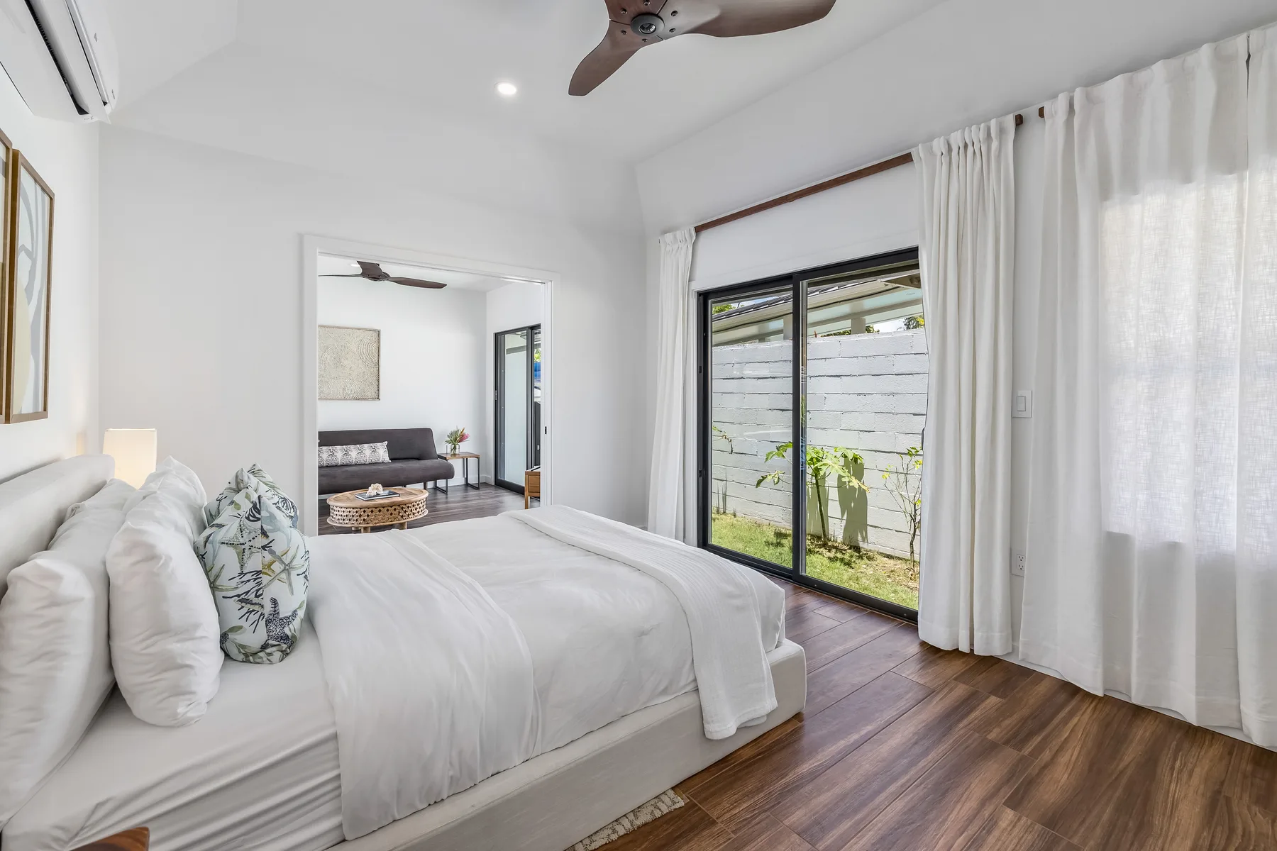 A bright bedroom with a bed beside sliding glass doors and curtains.