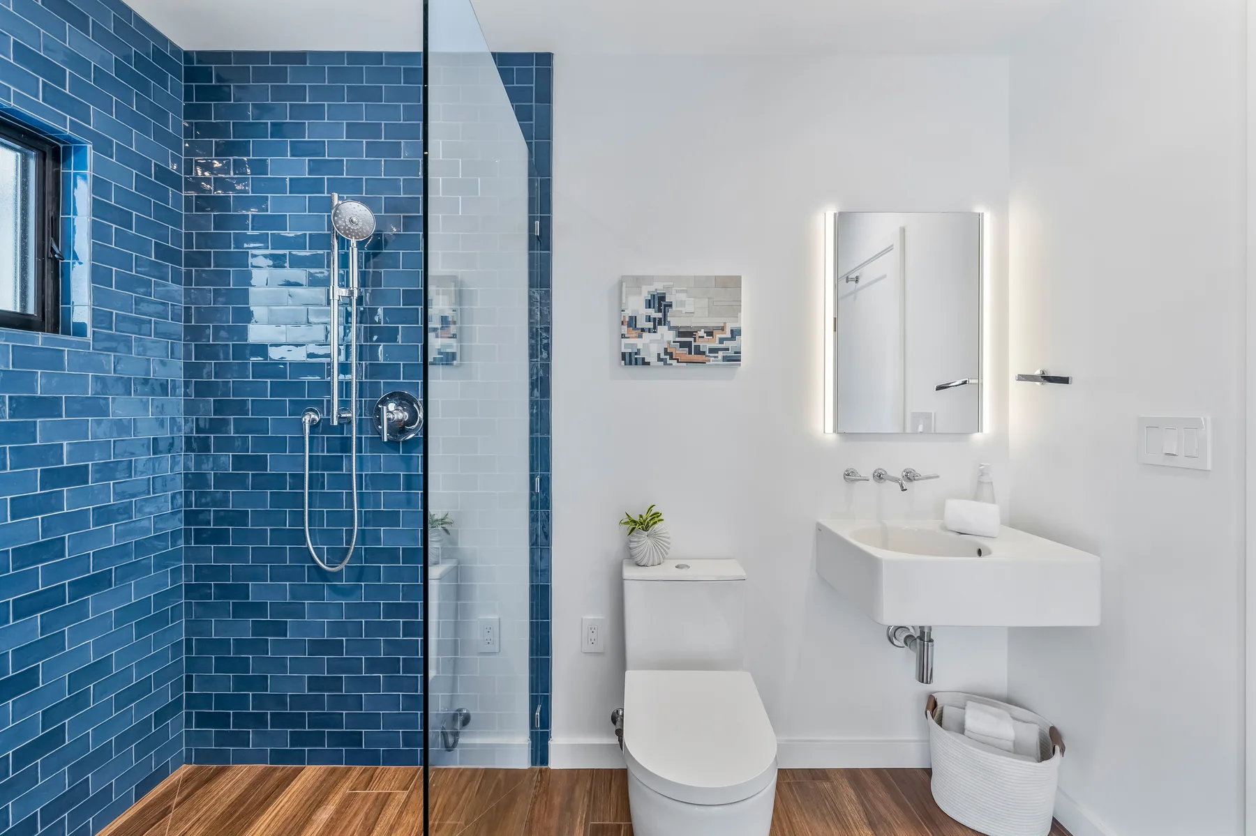 A modern bathroom with a blue-tiled shower and a white sink.