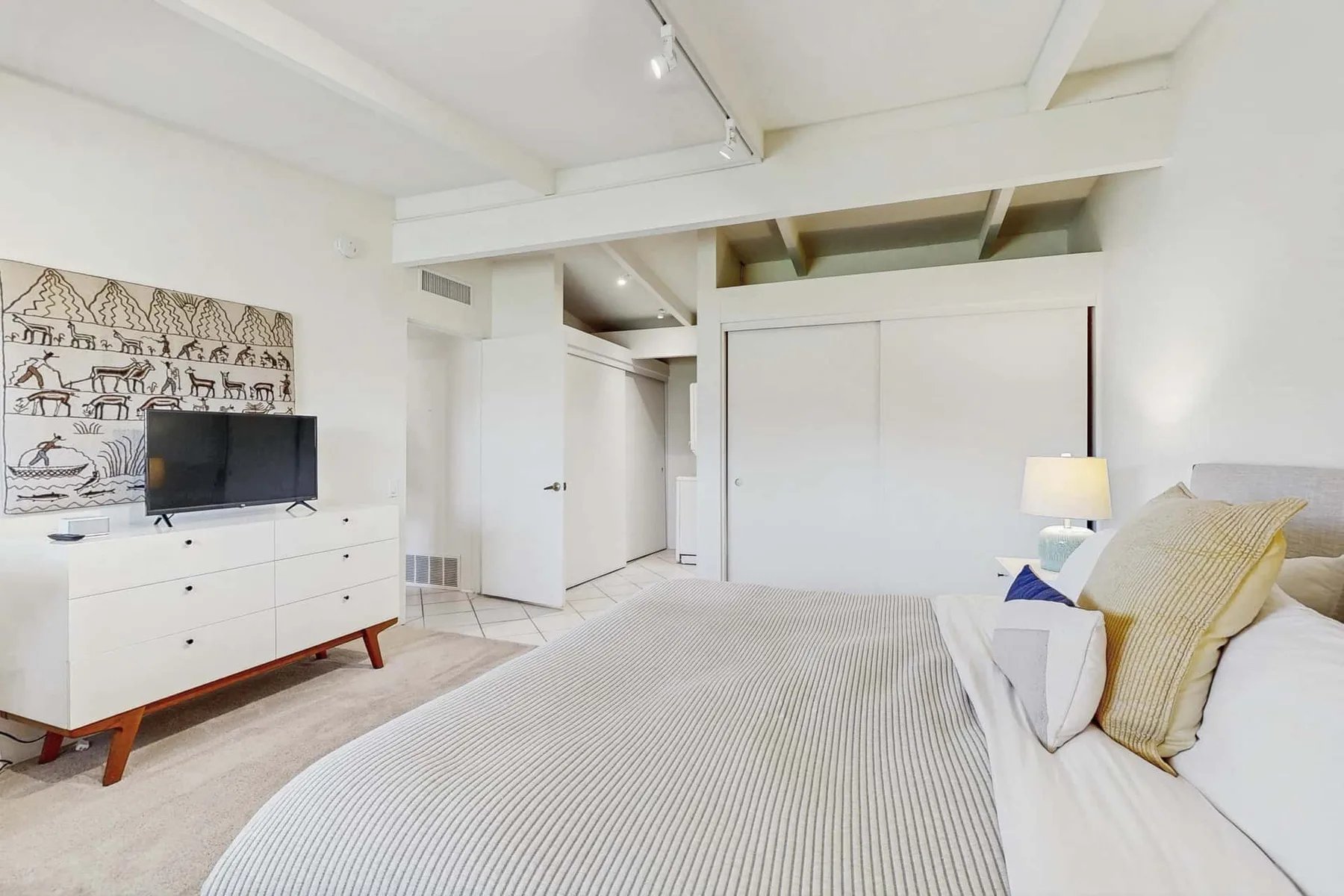 A bright bedroom with a bed, white dresser, and television.