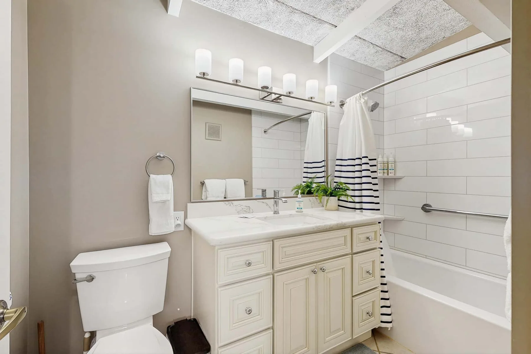 A bathroom with a vanity, sink, and bathtub behind a striped shower curtain.