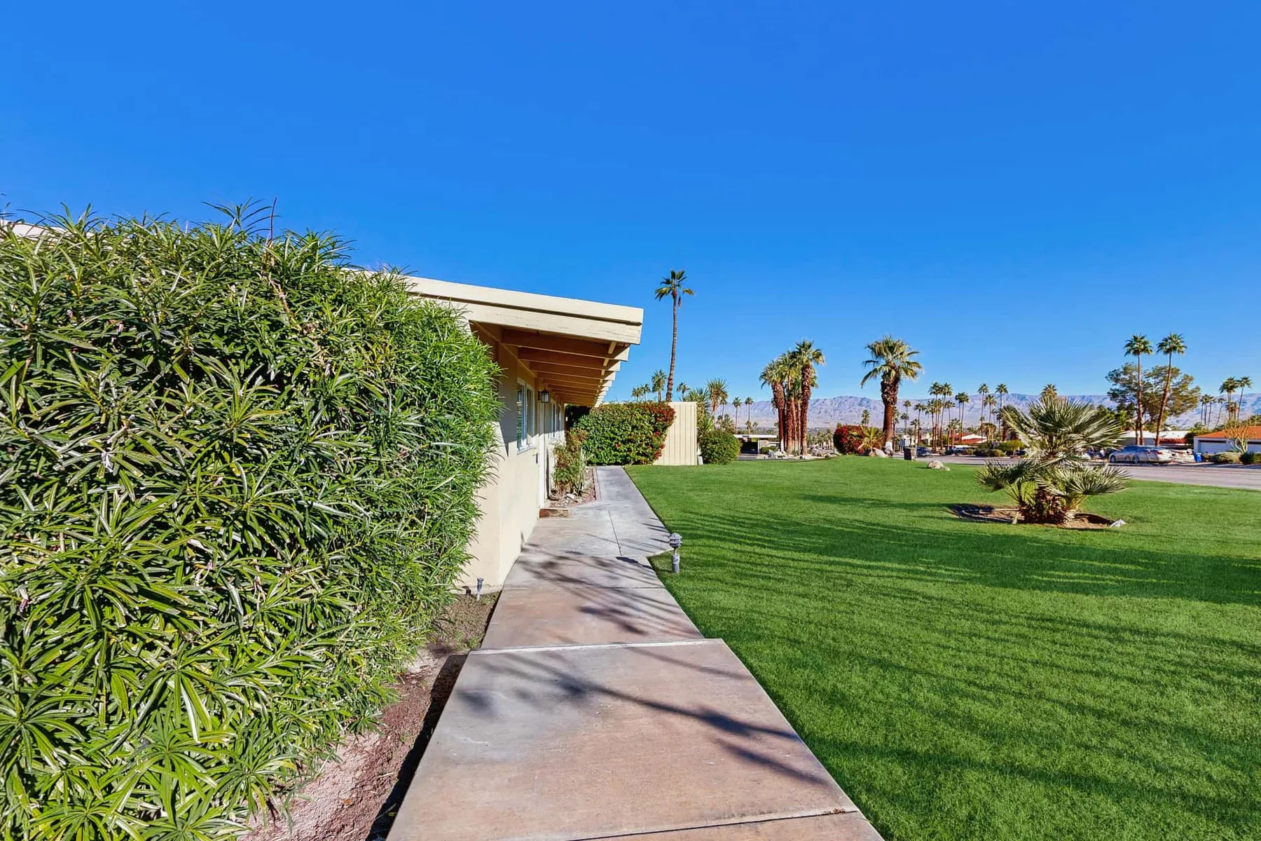 A paved walkway runs beside a hedge and expansive green lawn.