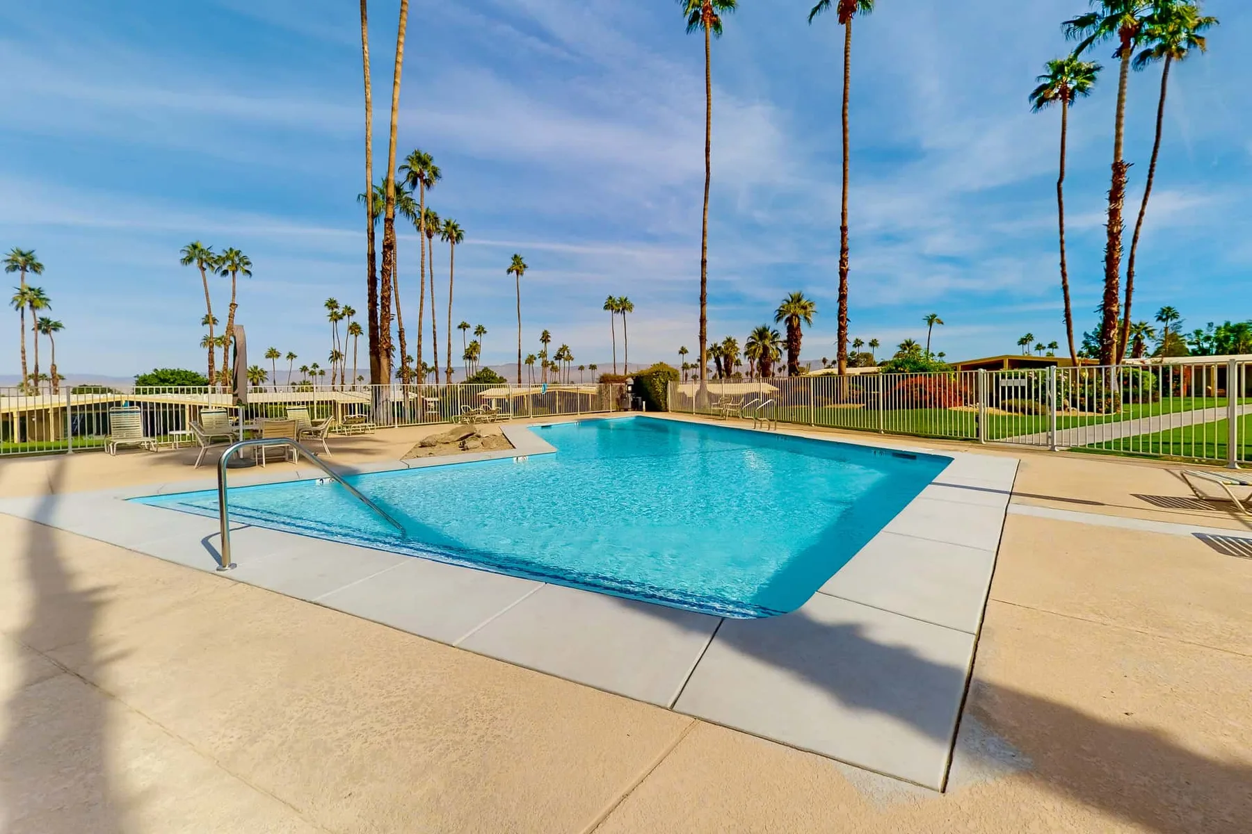 An outdoor swimming pool is surrounded by a paved deck and palm trees.