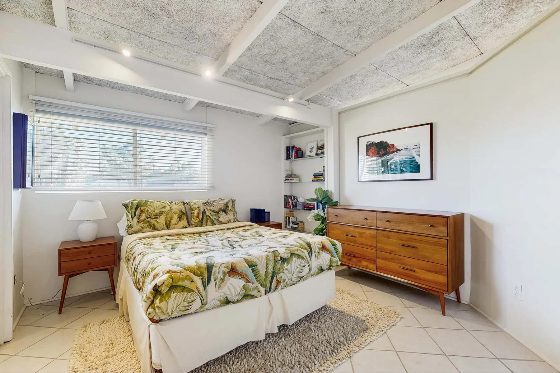 A bedroom with a bed covered in leafy-patterned bedding and wooden furniture.