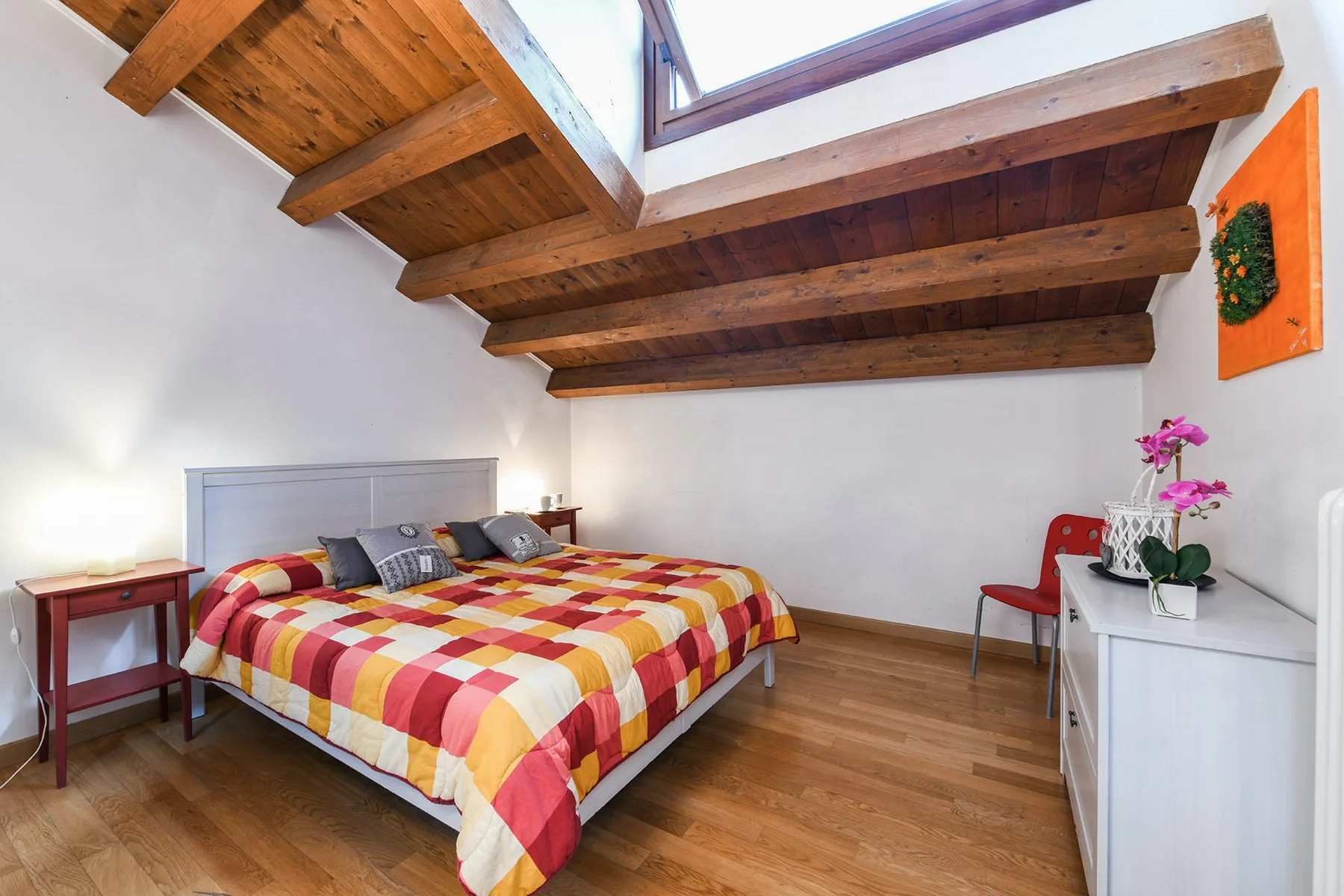 Un dormitorio con una cama colorida bajo vigas de madera expuestas en el techo.