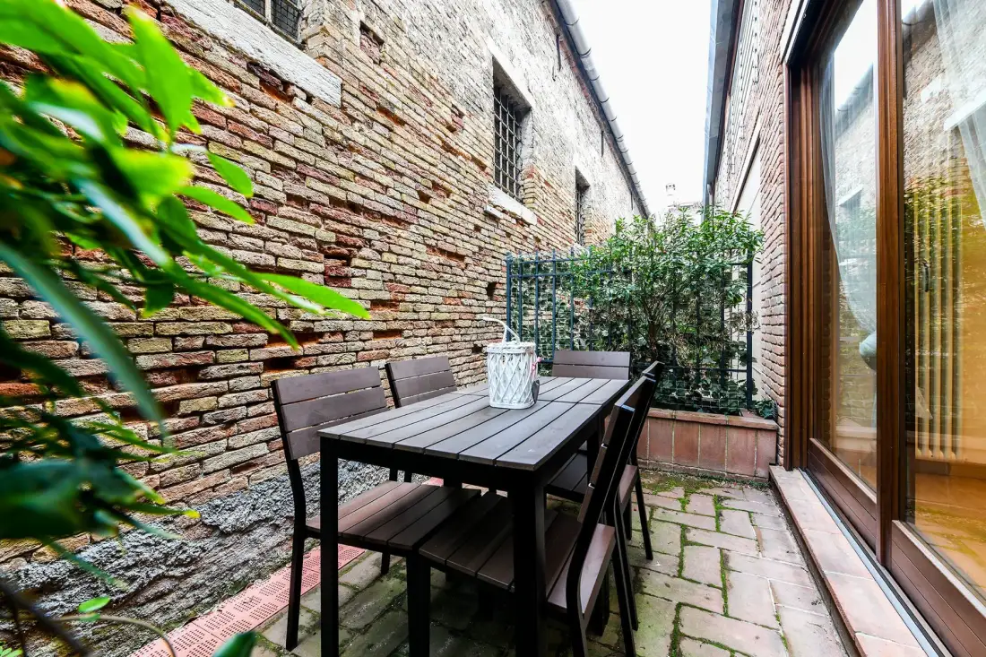 Un pequeño patio de ladrillo con una mesa y asientos al aire libre junto a puertas de vidrio.