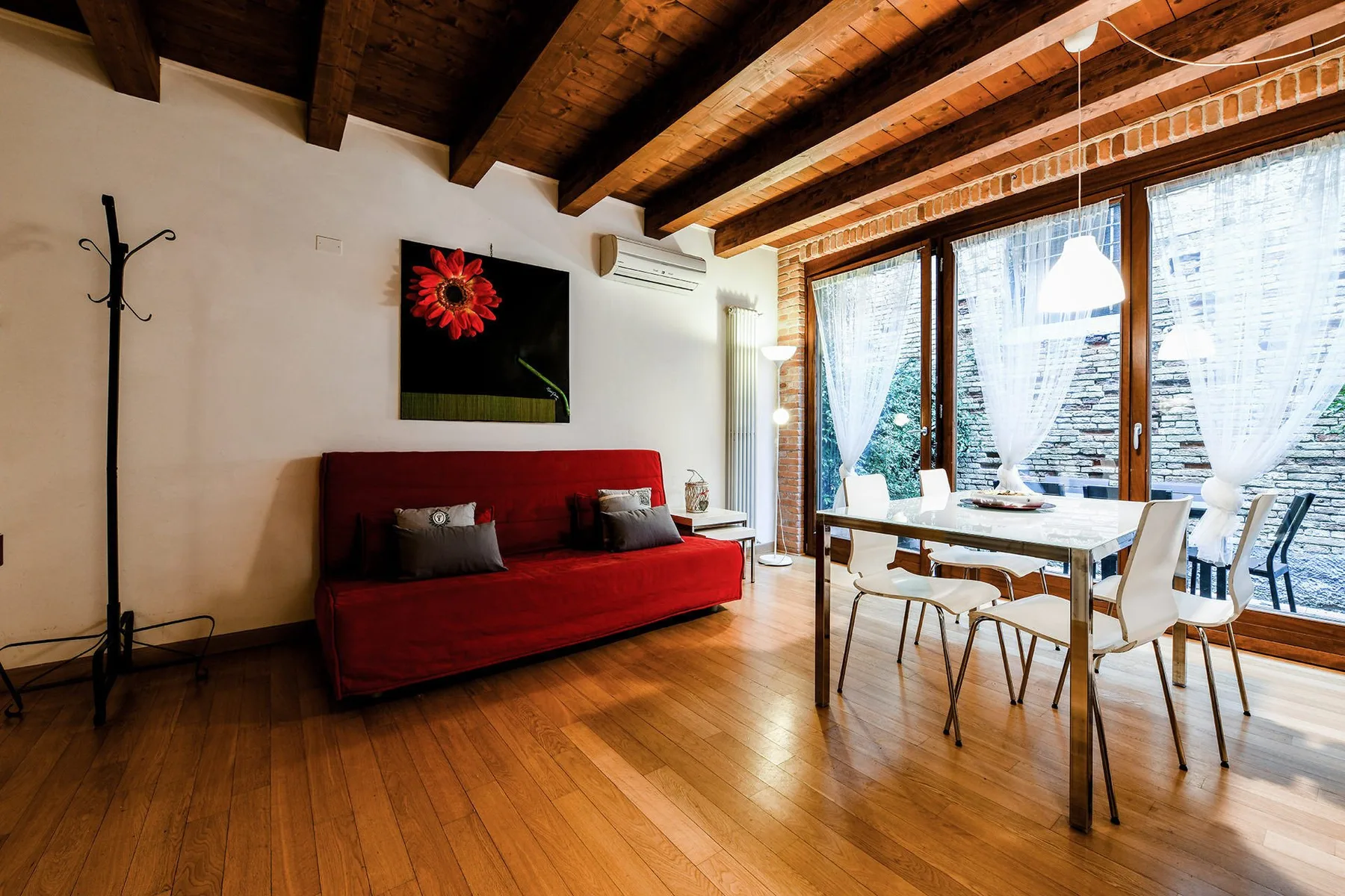 Una luminosa sala de estar y comedor con asientos rojos junto a grandes ventanas con cortinas.