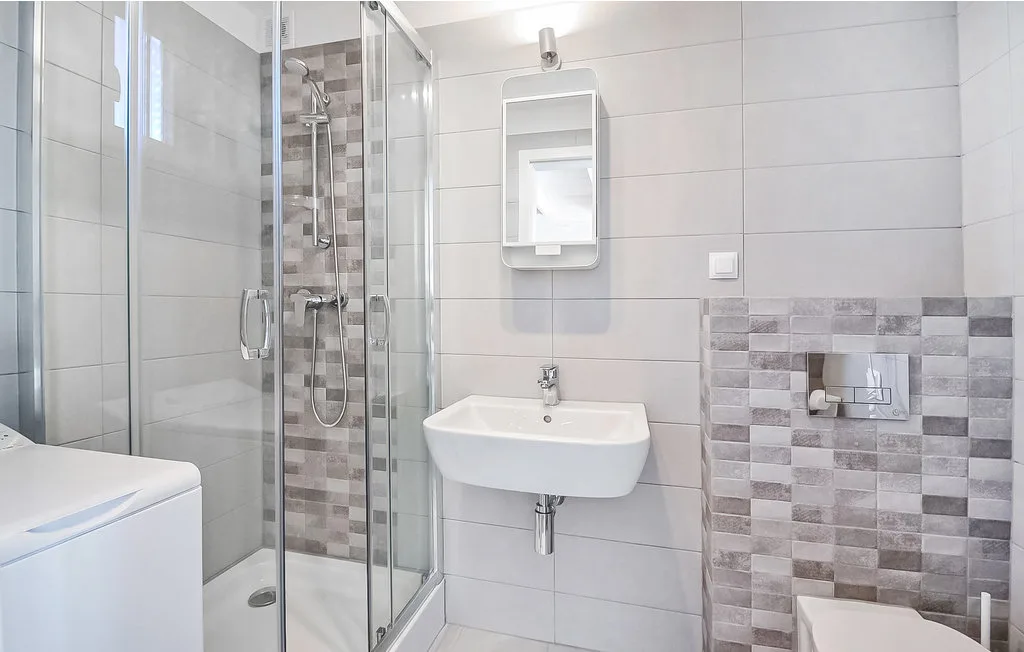 Un baño con azulejos, ducha de vidrio, lavabo de pared e inodoro.