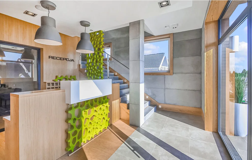 Un mostrador de recepción está junto a una escalera en un vestíbulo luminoso con grandes ventanas.