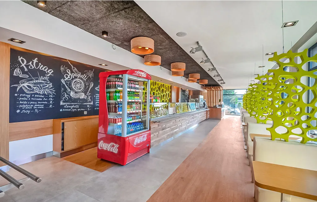 Una cafetería luminosa con una nevera de bebidas y un menú en pizarra.
