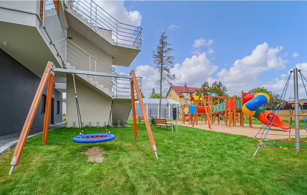 Un parque infantil al aire libre junto a un edificio, con columpios y juegos coloridos sobre el césped.