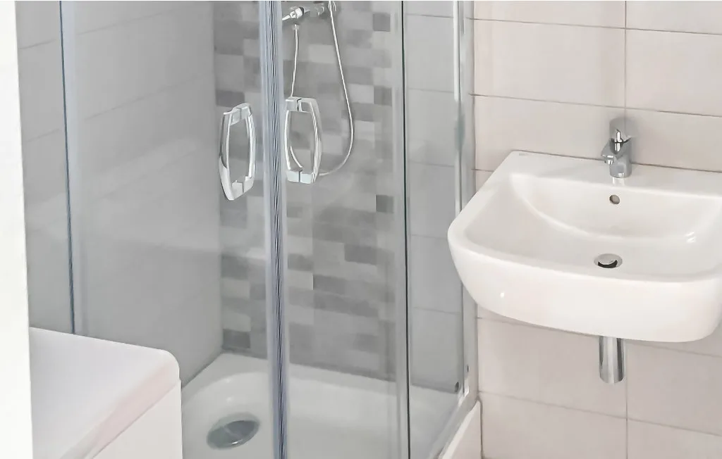 Un baño con una ducha de vidrio y un lavabo de pared.