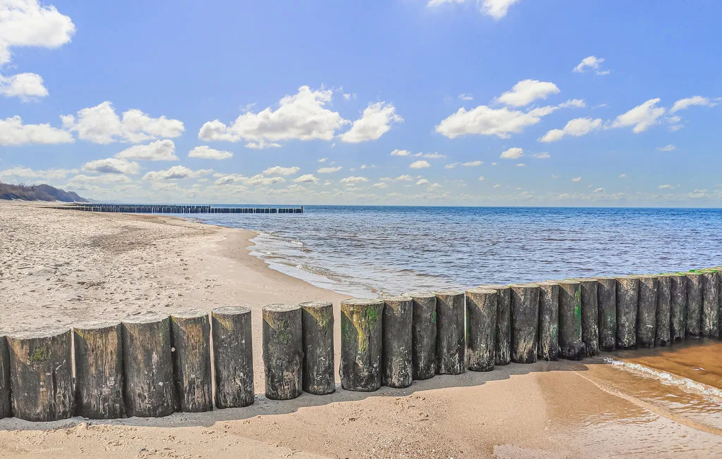Una playa de arena se une al agua tranquila detrás de una fila de postes de madera.