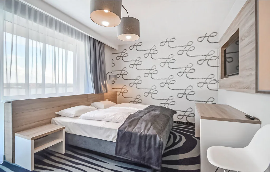 Un dormitorio con una cama, papel tapiz estampado y una ventana grande con cortinas.