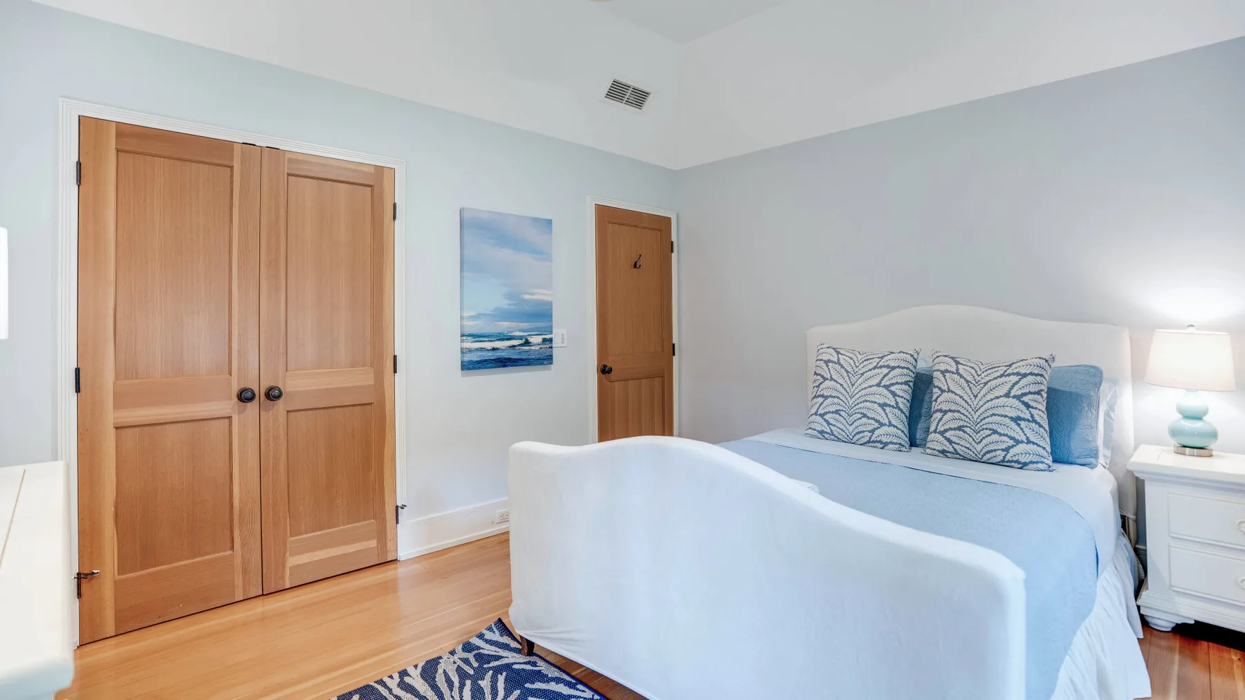 A bedroom with a bed, wooden closet doors, and a coastal wall print.