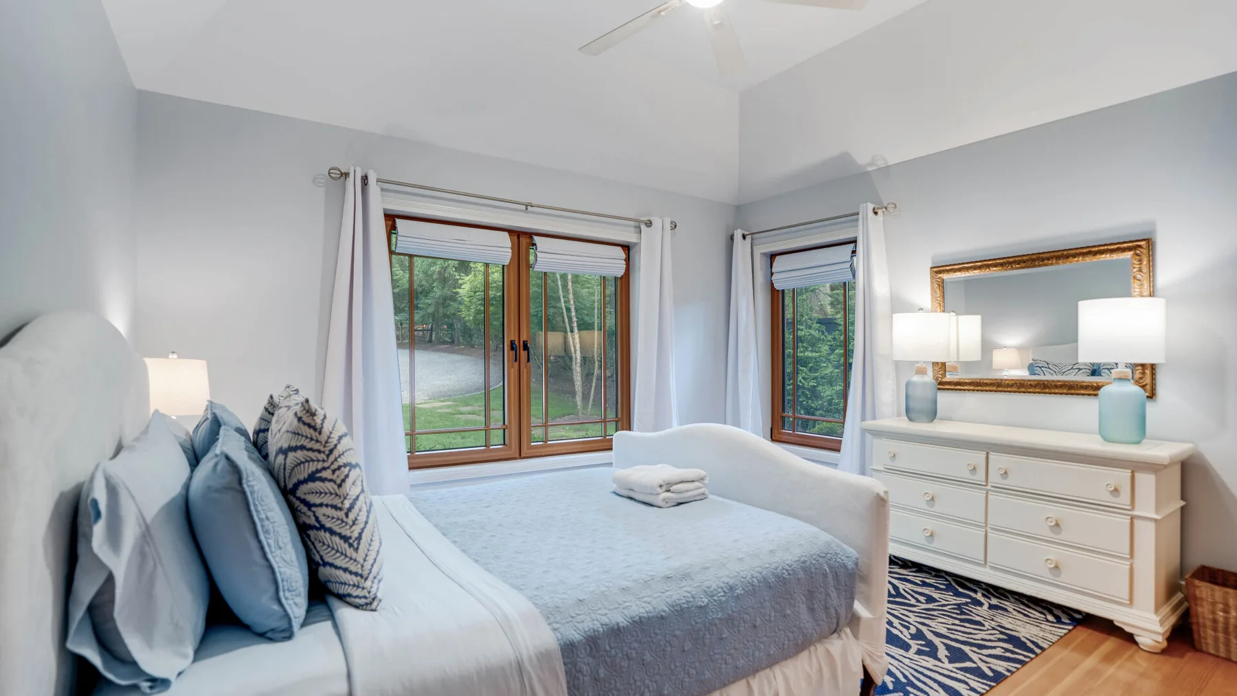 A bedroom with a bed, bedside lamp, and dresser beside the window.