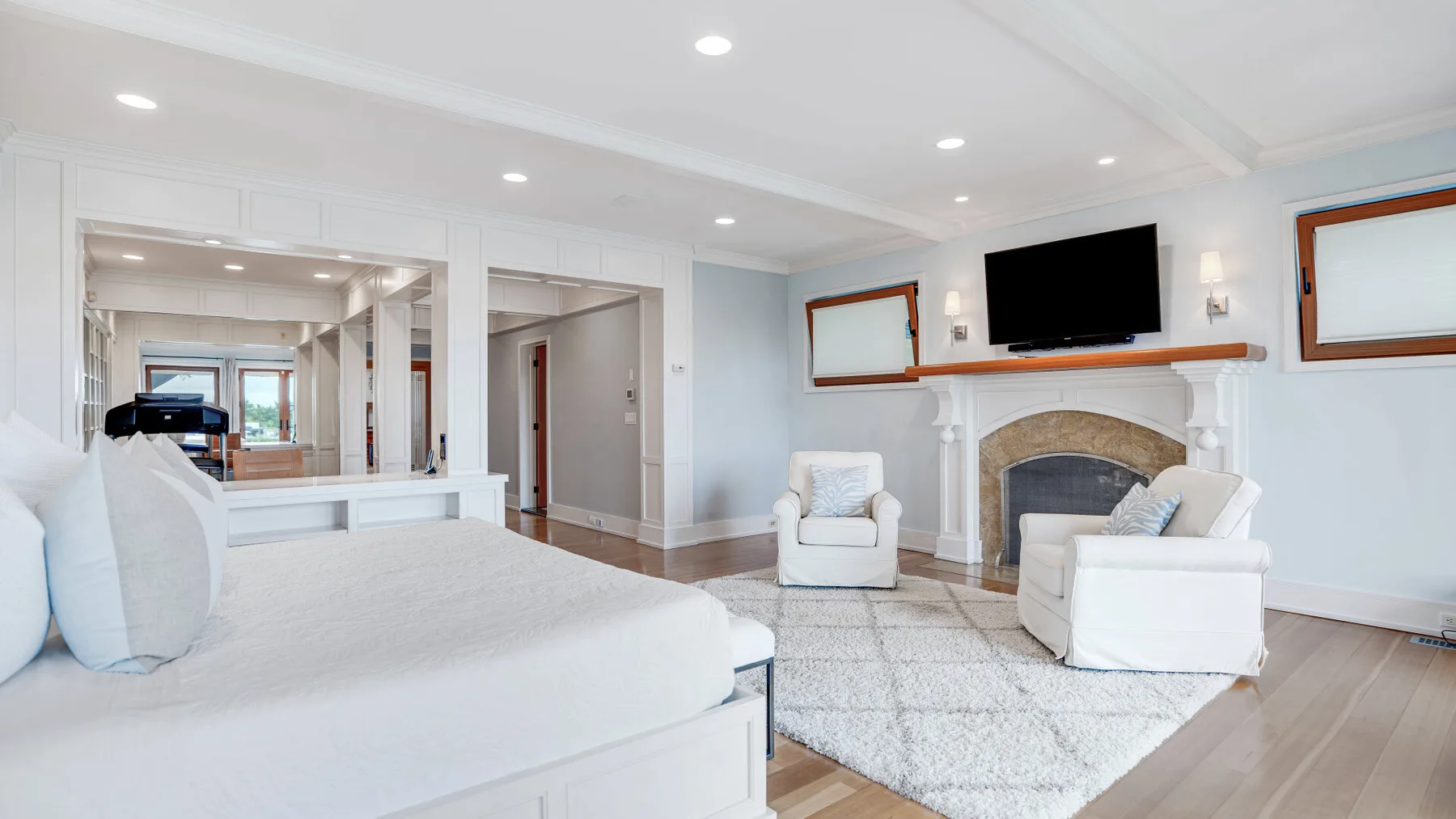 A bright living room with white seating, a fireplace, and a wall-mounted television.