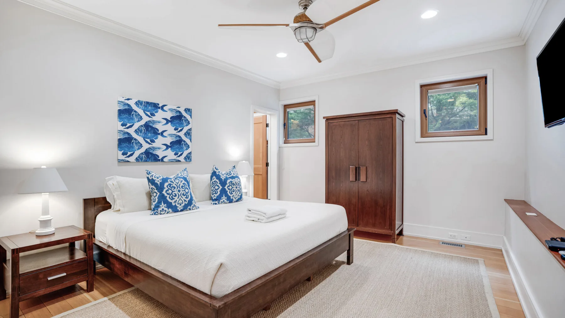 A bedroom with a neatly made bed, blue patterned cushions, and a wooden wardrobe.