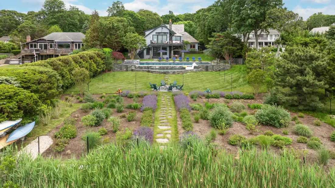 A landscaped garden path leads toward a house and swimming pool.