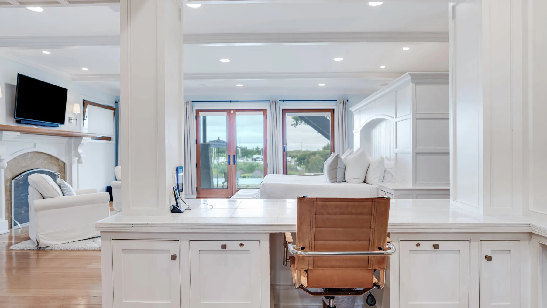 A bright living room with white seating and a wooden chair at a built-in desk.