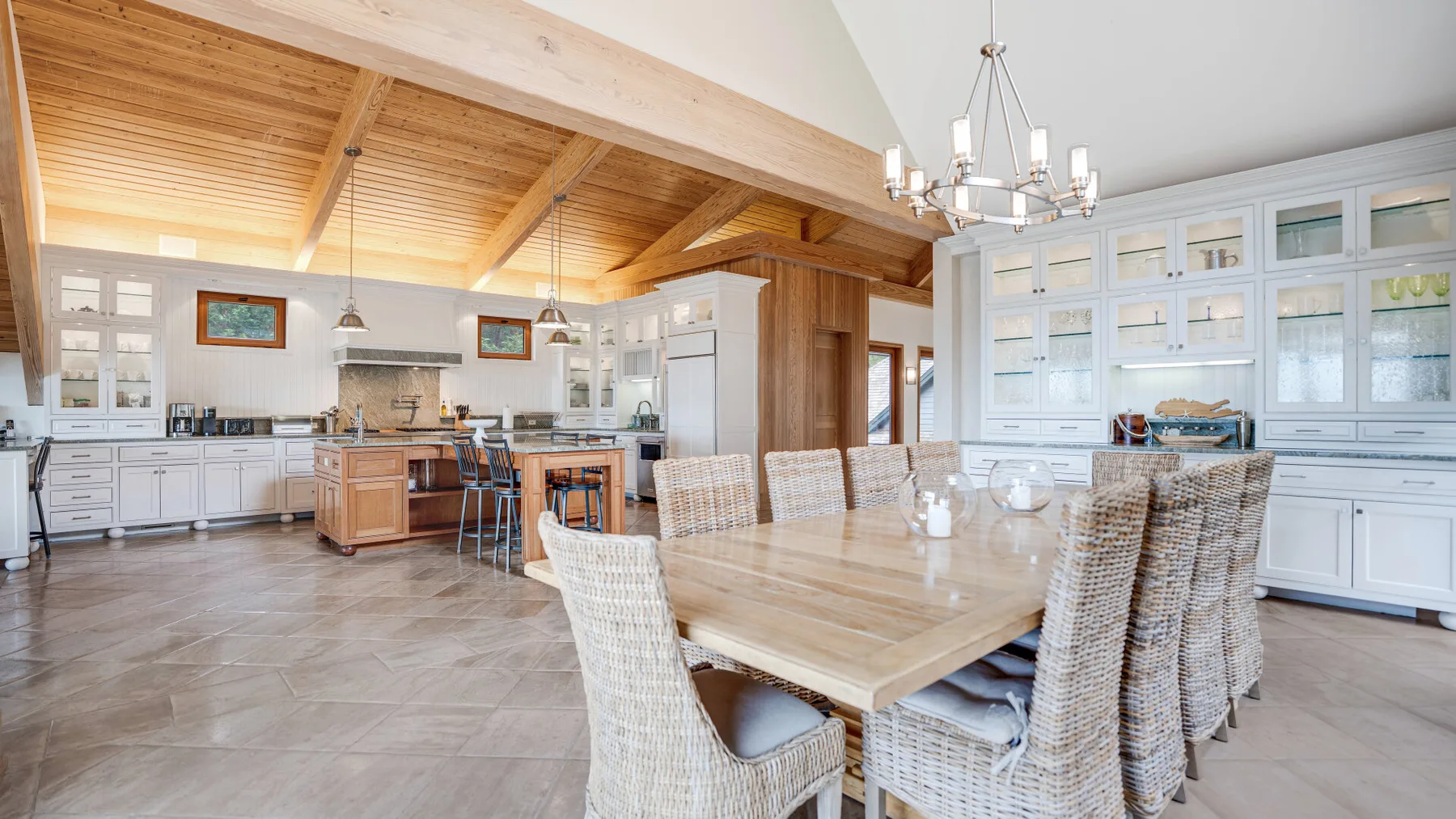 A bright open dining and kitchen area with a large table beneath a wood ceiling.