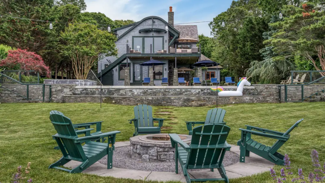 A landscaped yard with green seating around a circular stone fire pit.