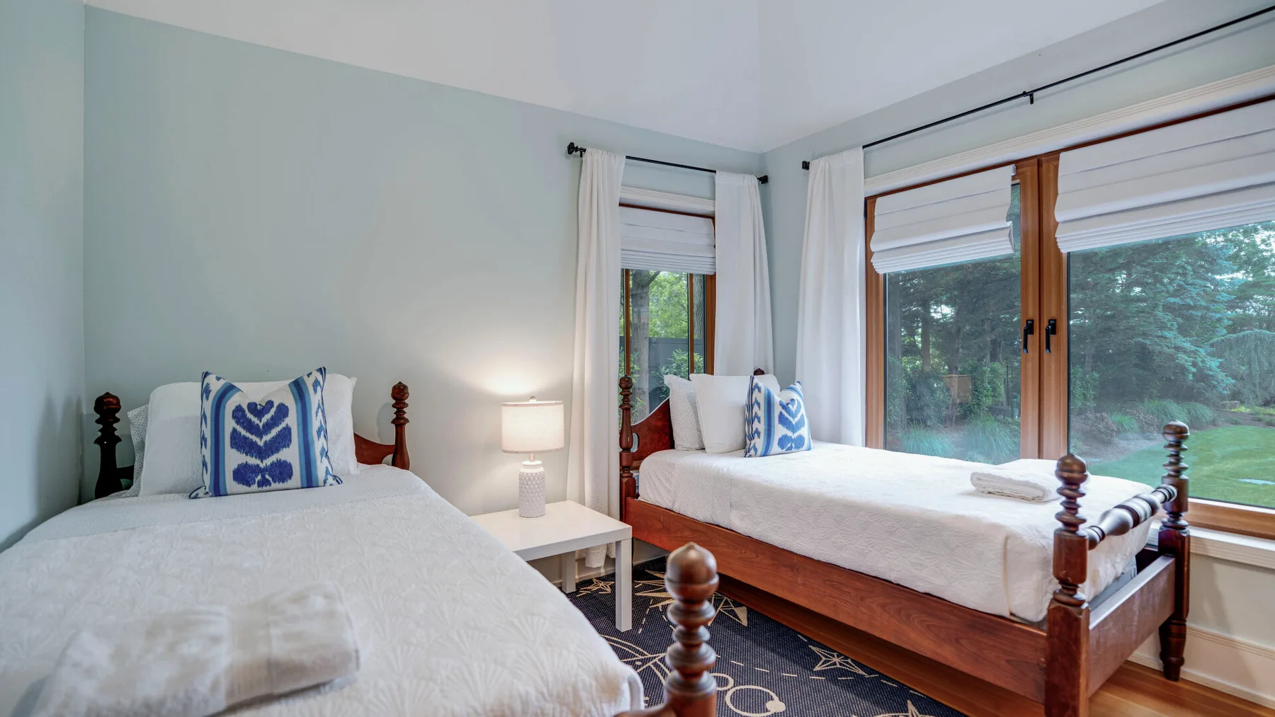 A bedroom with two beds, white bedding, and large windows.