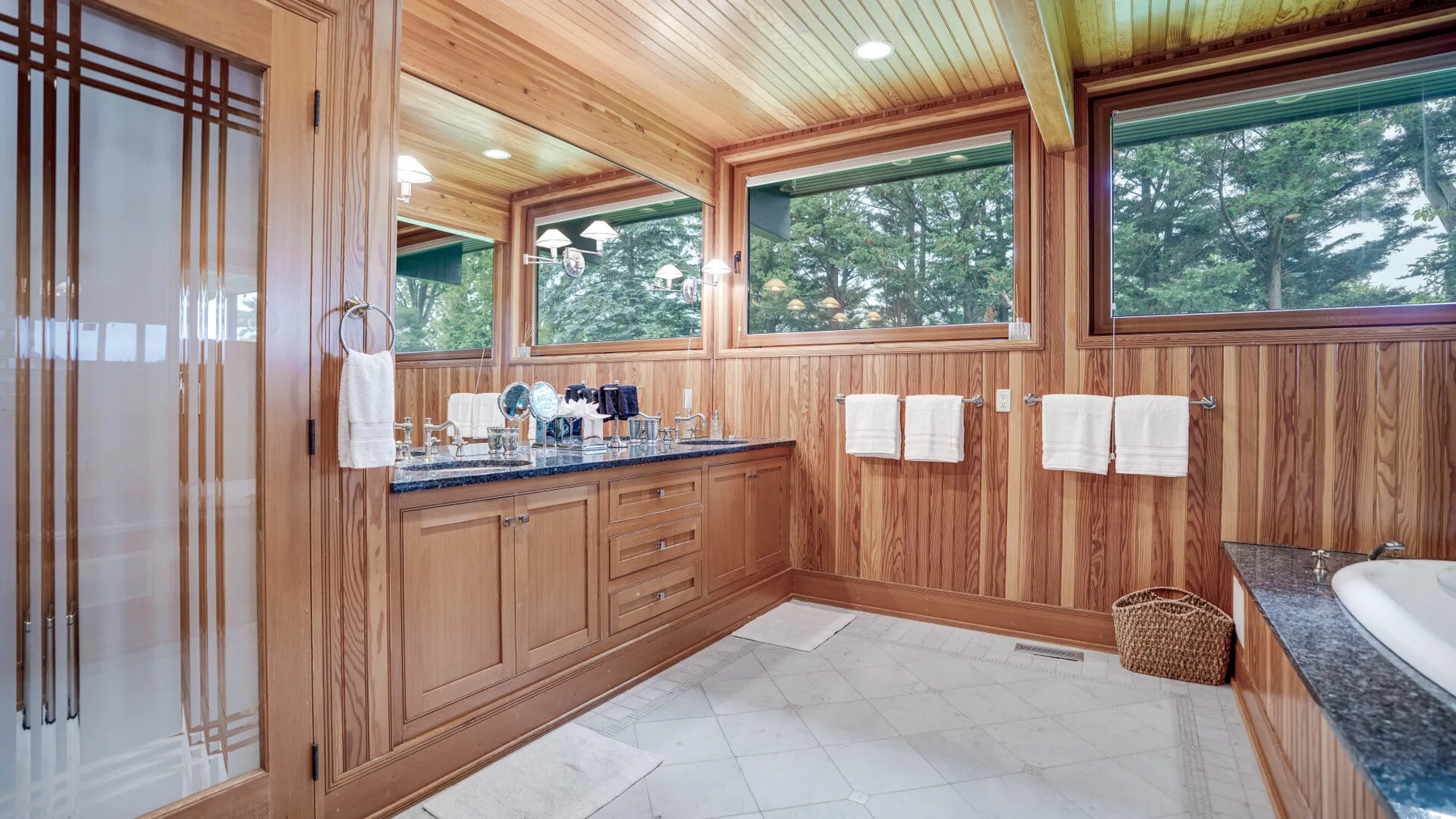 A wood-paneled bathroom with a long vanity, large windows, and a bathtub.
