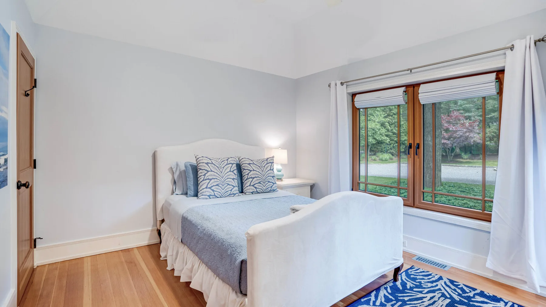 A bedroom with a bed beside a large window overlooking greenery.