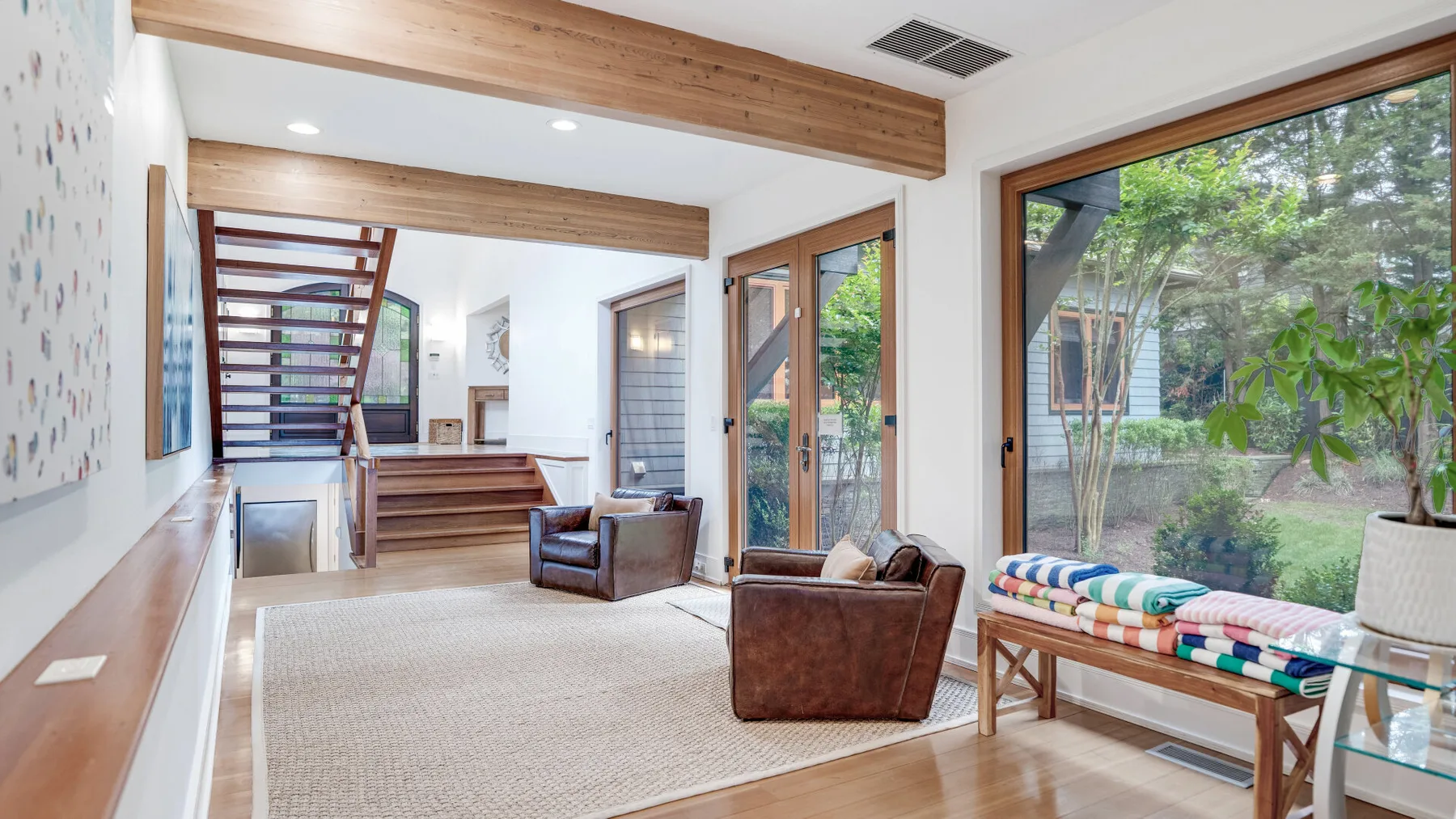 A bright living room with broad windows and a wooden staircase.