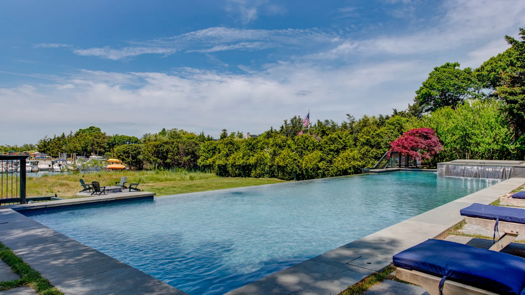 An outdoor swimming pool is surrounded by greenery and a blue sky.