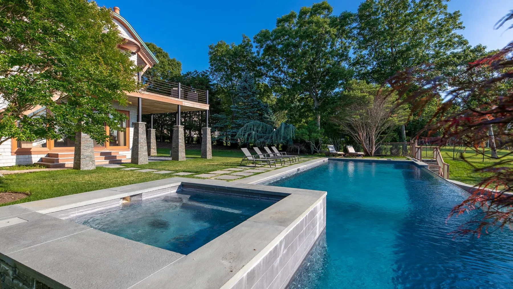 A swimming pool beside a raised spa, surrounded by trees and outdoor seating.