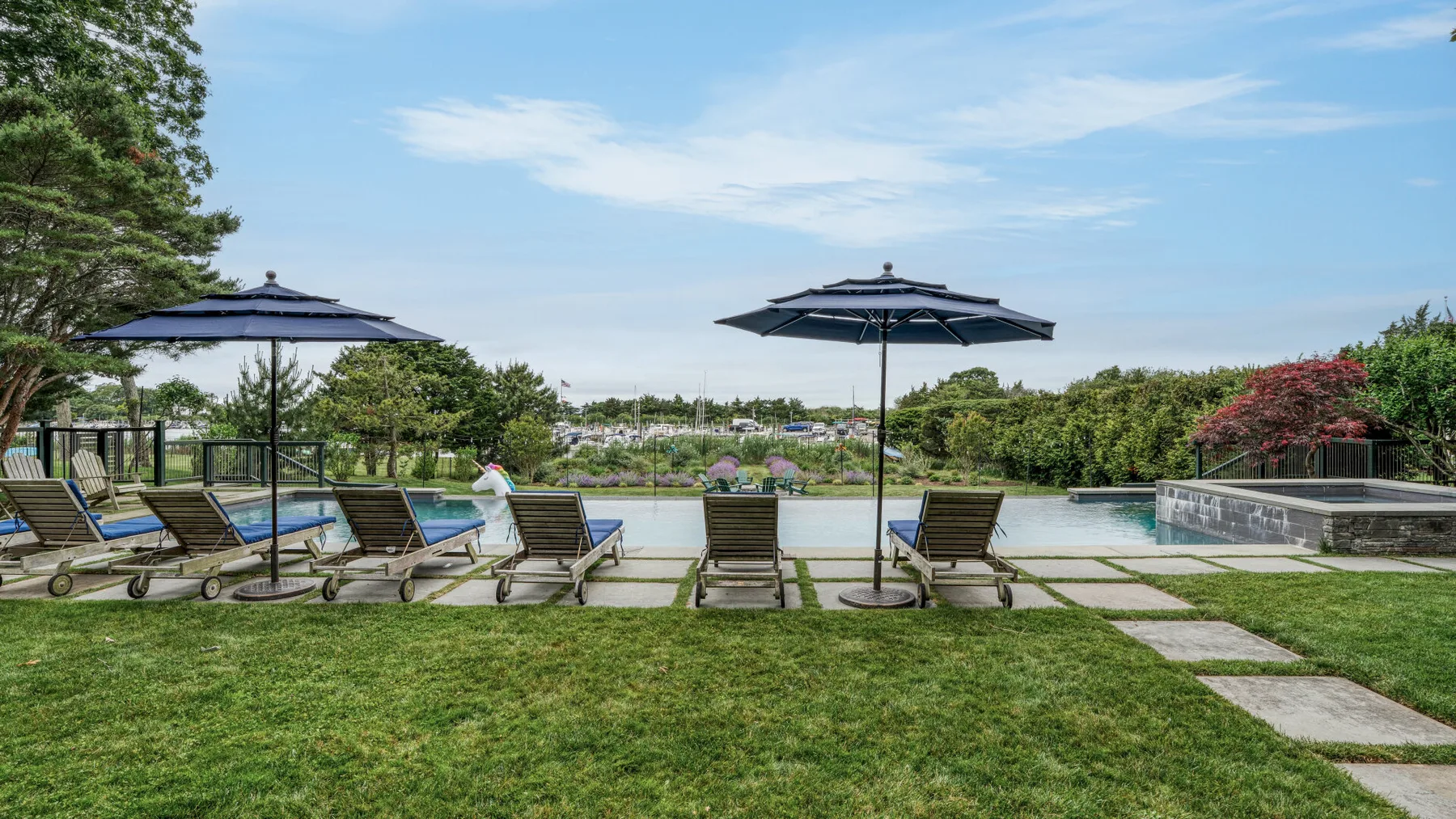 Outdoor poolside seating faces a swimming pool beneath dark umbrellas.