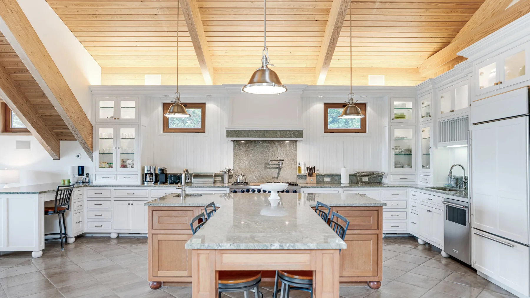 A bright kitchen with a large central island beneath a wood-paneled ceiling.