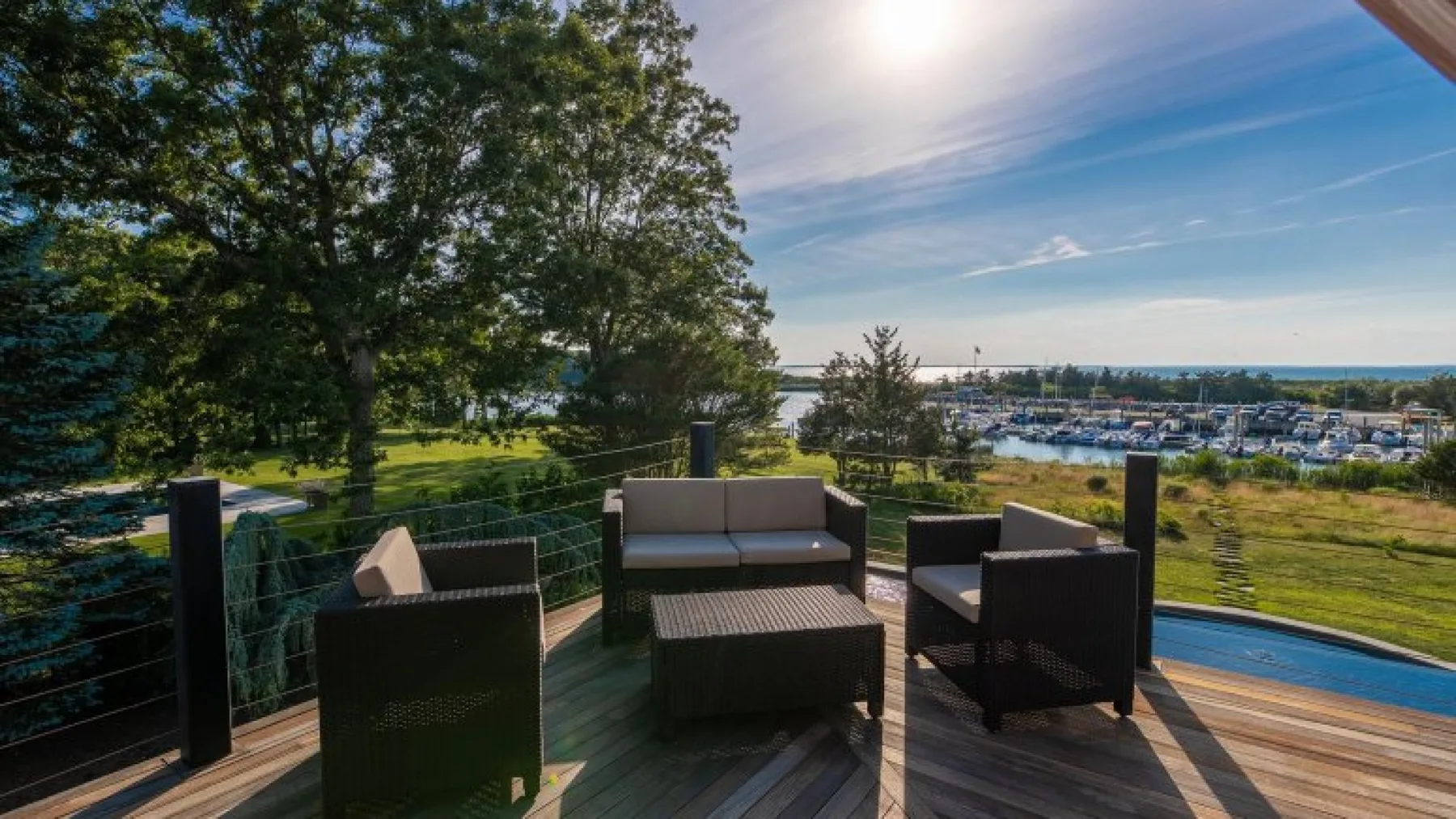 A wooden deck with outdoor seating overlooks the water and a marina.