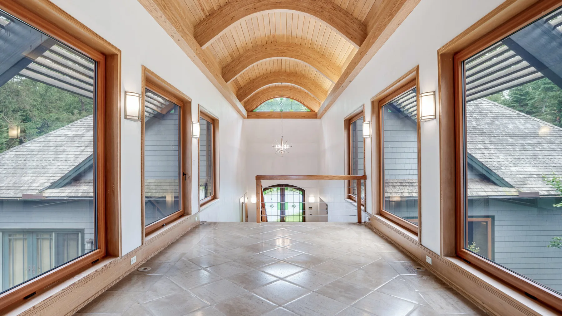 A bright hallway with a tiled floor, large windows, and a curved wooden ceiling.