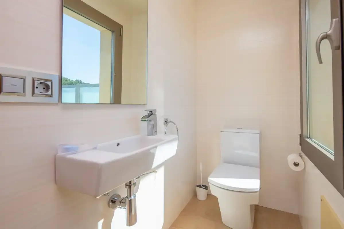 Un baño con lavabo suspendido, espejo e inodoro.
