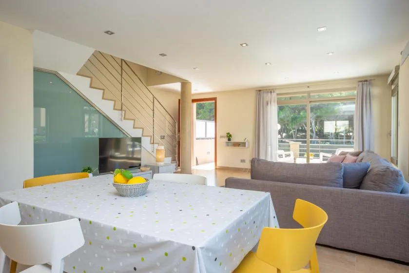 Una luminosa sala de estar y comedor con una mesa, sillas amarillas y una escalera.