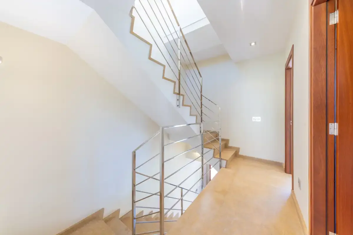 Un pasillo interior con una escalera y una barandilla metálica.