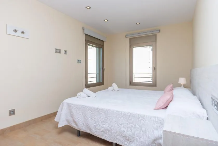 Un dormitorio luminoso con ropa de cama blanca y ventanas con vistas al exterior.