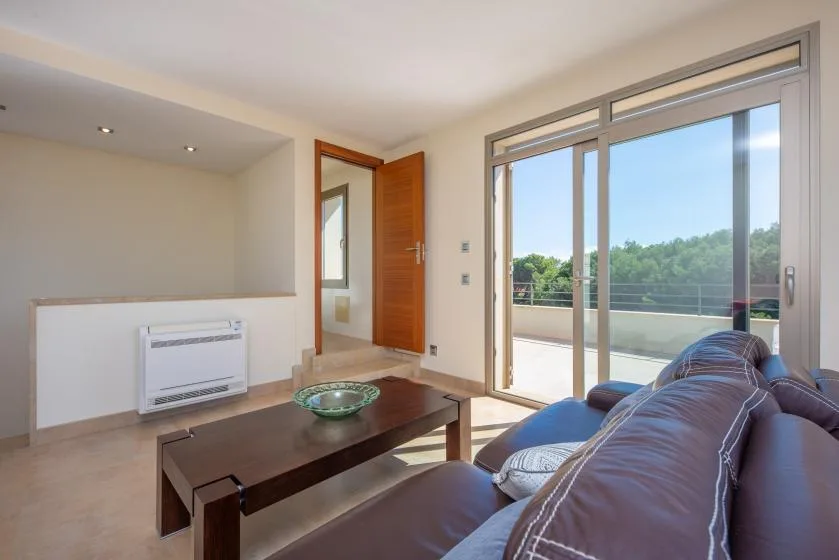Una sala de estar con asientos, una mesa de centro y puertas corredizas de vidrio hacia un balcón.