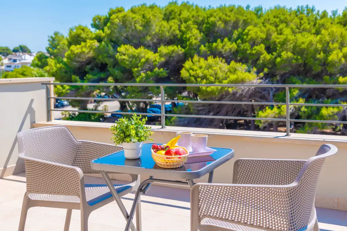 Una terraza al aire libre con una mesa, asientos y árboles detrás de la barandilla.