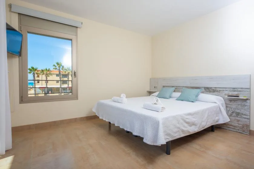 Dormitorio con una cama bien hecha y una ventana con vistas a edificios cercanos.