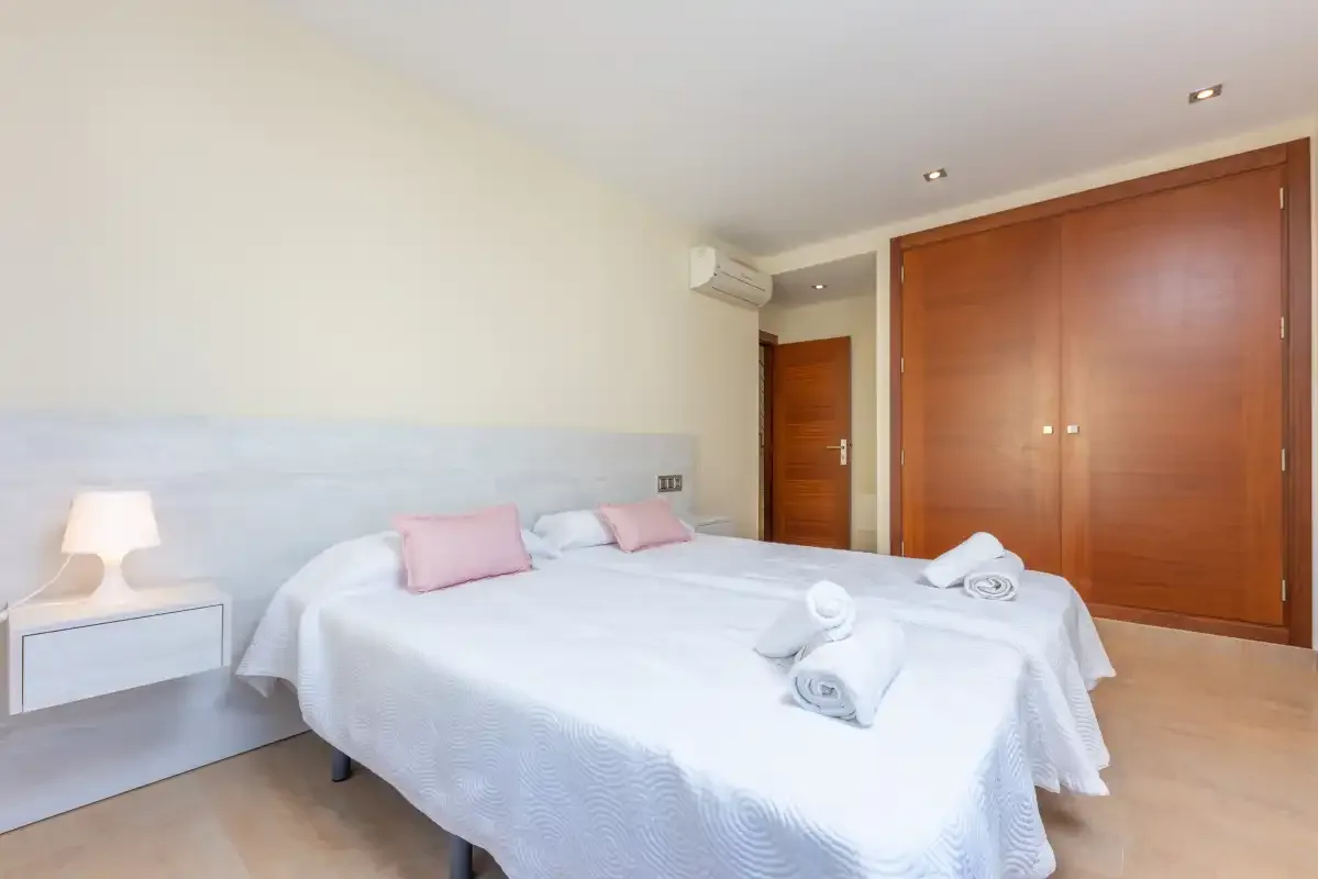 Un dormitorio luminoso con una cama blanca, una mesita de noche y armarios de madera.
