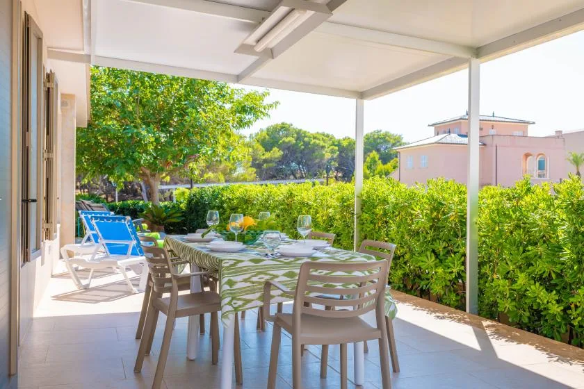 Comedor en un patio cubierto, con mesa y asientos junto a un seto frondoso.