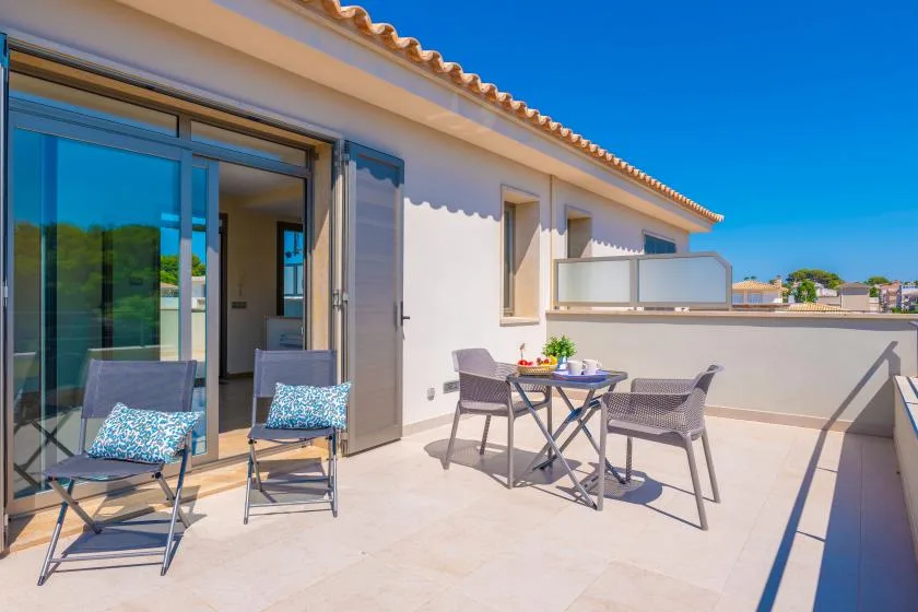 Una terraza soleada con asientos exteriores y una mesa junto a puertas corredizas de vidrio.