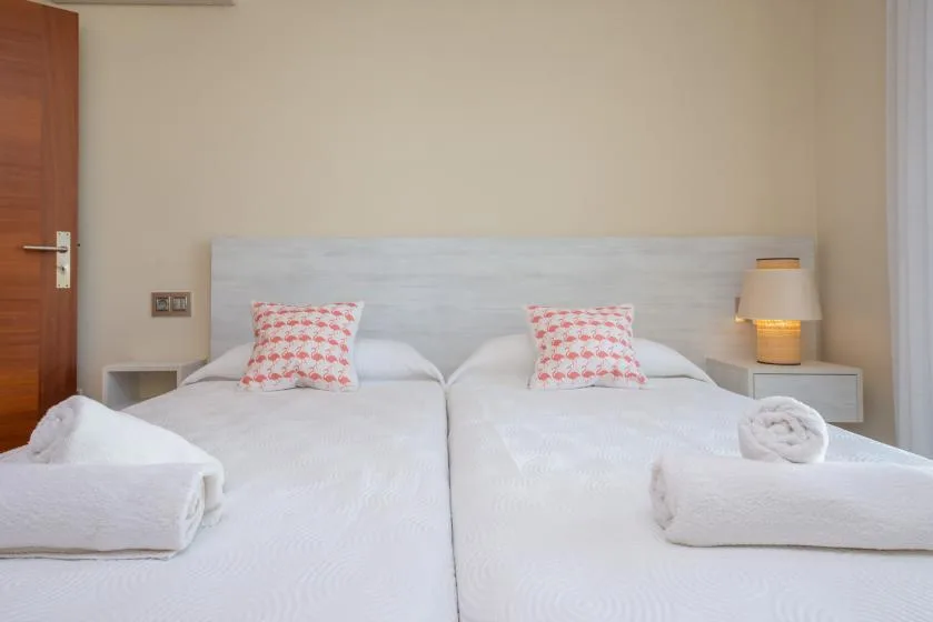 Un dormitorio con dos camas, cojines estampados y toallas dobladas.