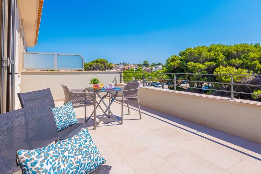 Una terraza soleada con asientos al aire libre, una mesa y vistas a los árboles.
