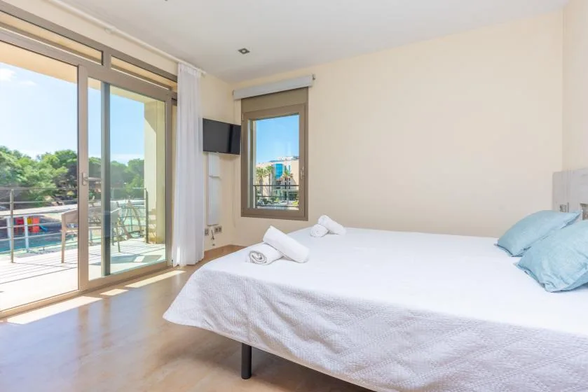 Un dormitorio luminoso con una cama junto a puertas corredizas de vidrio que dan a un balcón.