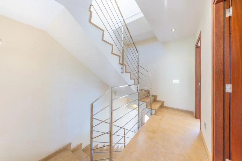 Una escalera interior luminosa con barandillas metálicas y un descansillo de baldosas.
